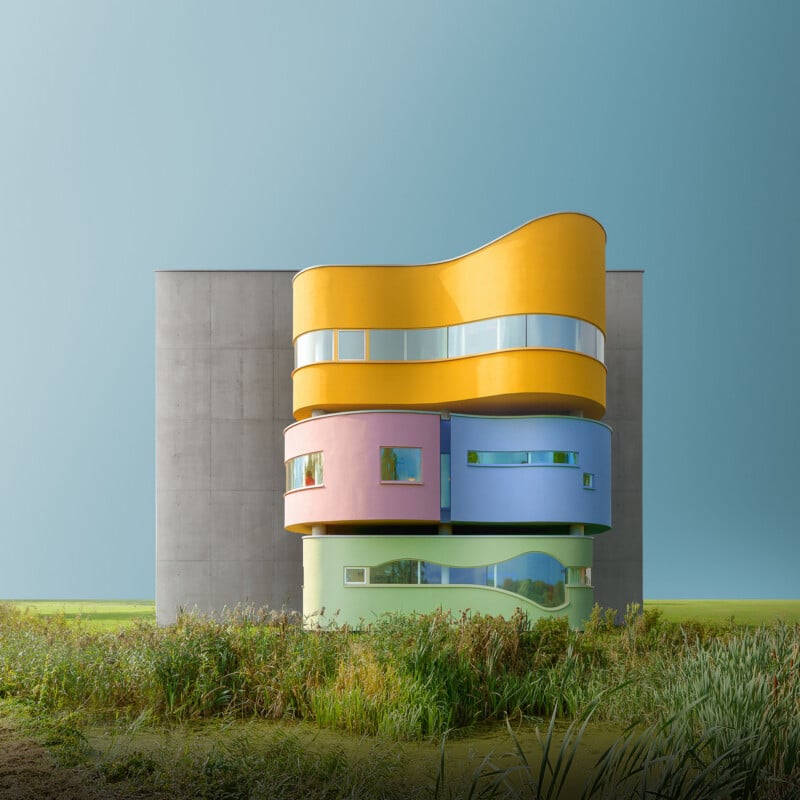 A modern building with a gray concrete facade features a central, multi-colored section of stacked, curved volumes in yellow, pink, blue, and green, set against a grassy landscape.