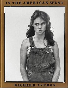 The cover of the book In the American West by Richard Avedon features a black-and-white portrait of a young woman with freckles wearing denim overalls.