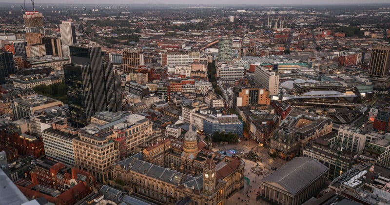 An aerial view of a dense city center featuring a historic clock tower building, modern skyscrapers, and a train station complex at dusk.