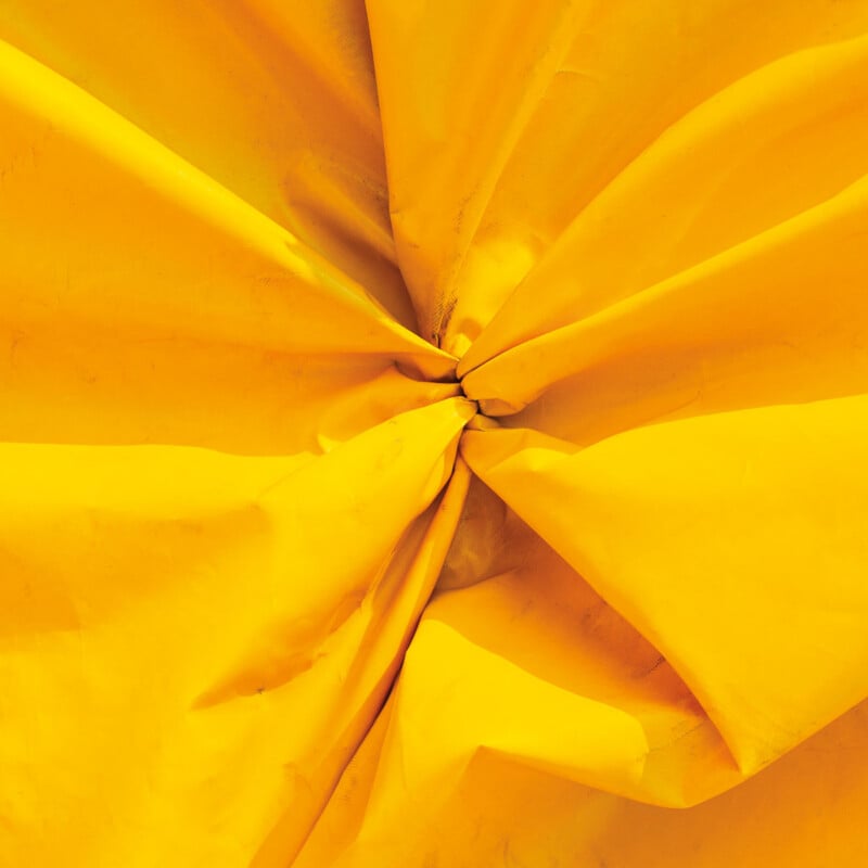 A close-up view of bright yellow fabric gathered and folded toward a central point, creating deep shadows and highlights.