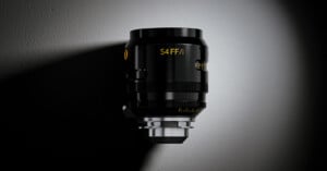 A black Cooke S4 FF/i cinema lens stands vertically against a dark, textured background with a spotlight effect.