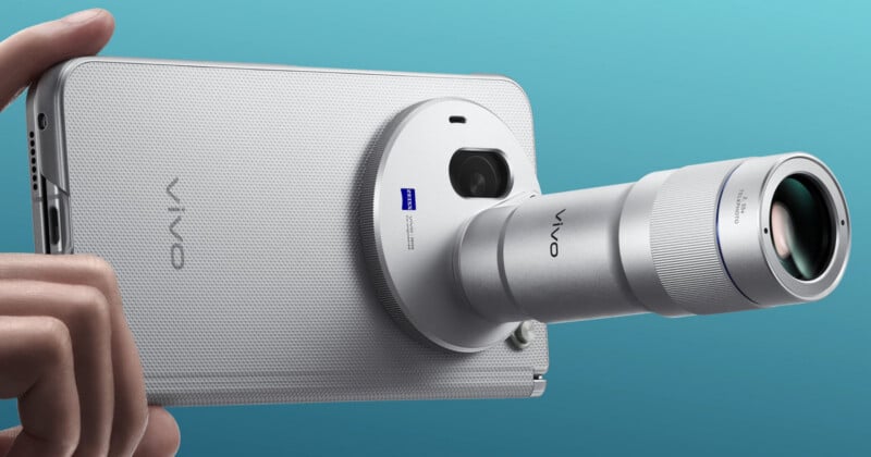 A hand holds a silver smartphone with a large, circular camera module attached to the back, featuring a prominent, protruding telephoto lens.
