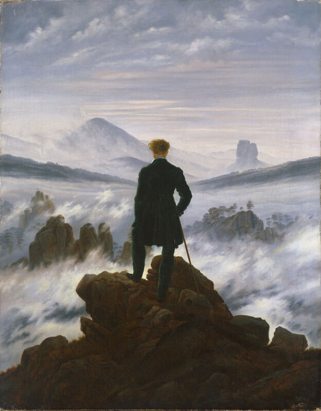 A man in a dark frock coat stands with his back to the viewer atop a rocky precipice, looking out over a sea of thick fog.