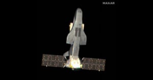 A spaceplane with extended solar panels is captured in orbit against a black background, with a bright light emanating from its rear section.