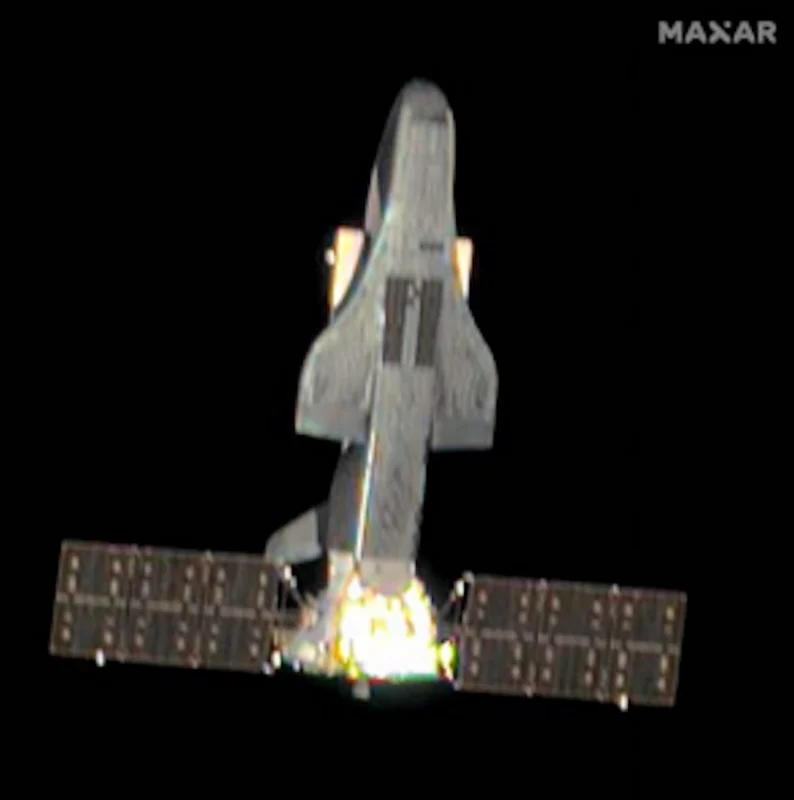 A space plane with extended solar panels in orbit, with a bright light visible at its base.