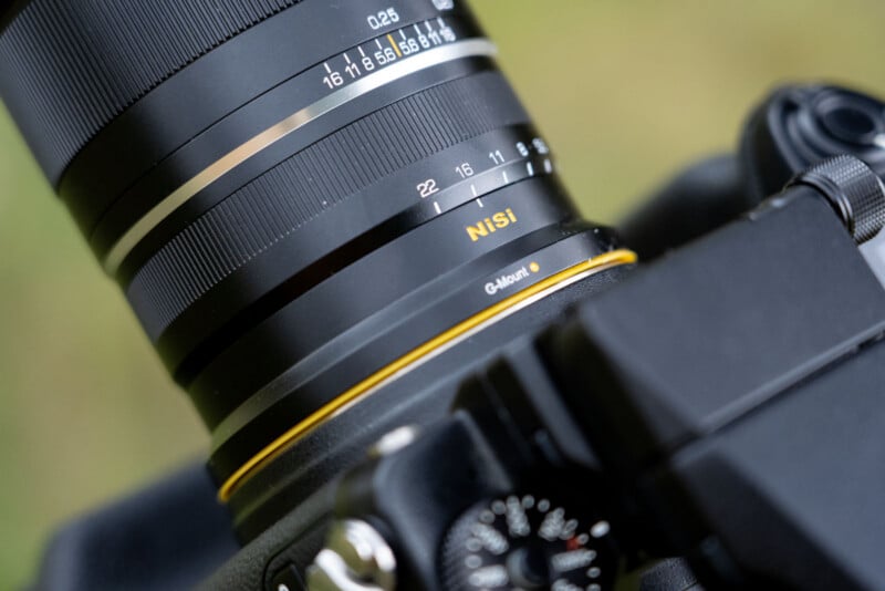 A close-up view of a camera lens with a manual aperture ring labeled "NiSi" and "G-Mount," attached to a black camera body.