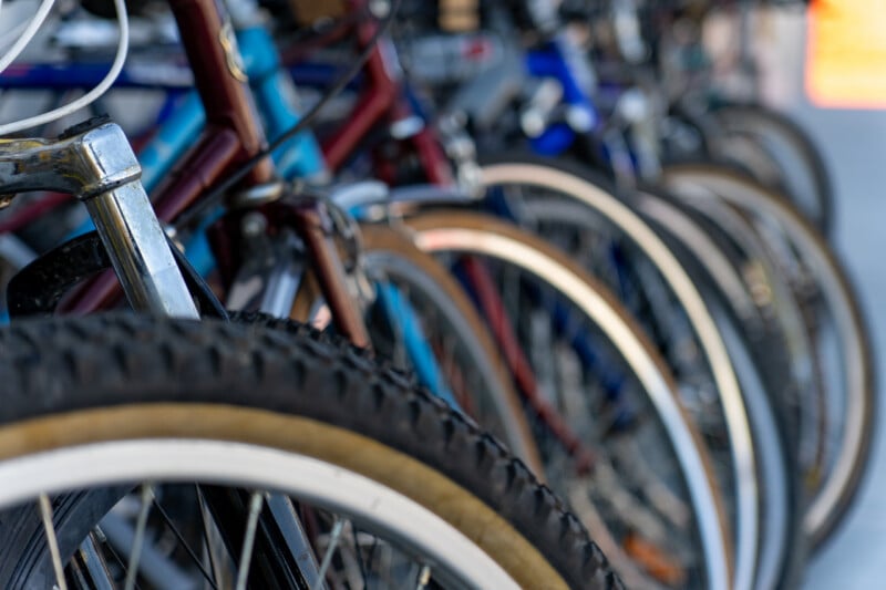 A row of bicycles parked in a line, with the front tire of the closest bike in sharp focus and the others receding into a soft blur.