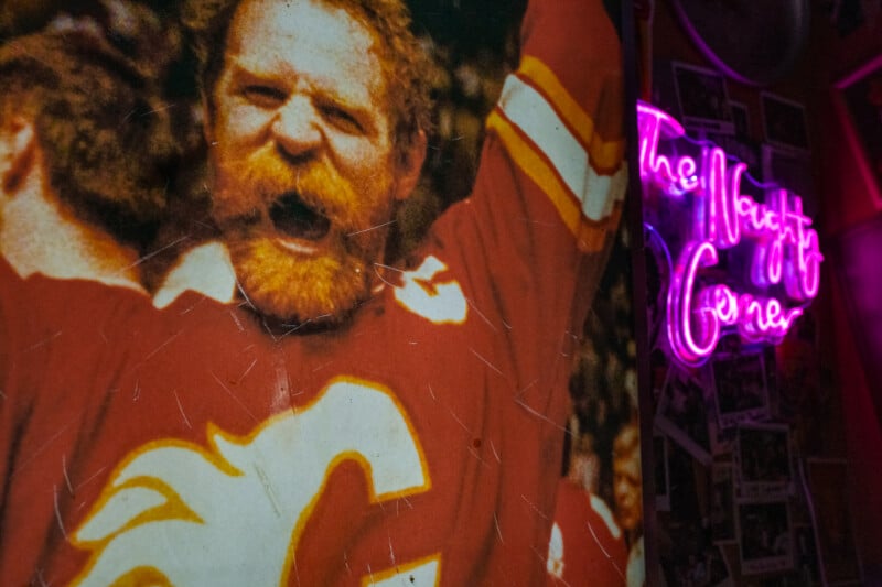 A close-up of a vintage poster featuring a bearded hockey player in a red Calgary Flames jersey, next to a pink neon sign that reads 