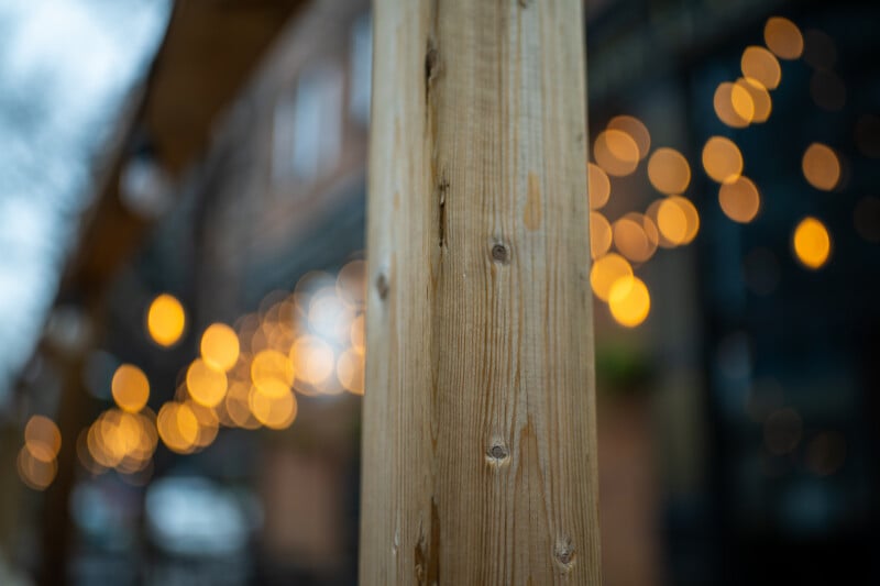 A vertical wooden post stands in the foreground, with blurred, out-of-focus string lights glowing in the background.