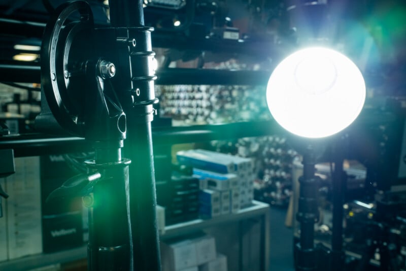 A close-up view of a black tripod head in the foreground with a bright, circular studio light glowing in the background.