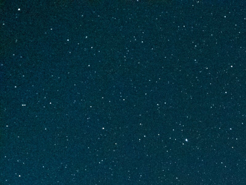 A dark blue, grainy background filled with numerous small, scattered white dots resembling stars.