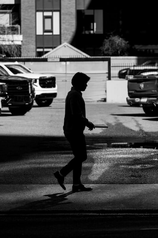 A silhouette of a person walking across a parking lot while holding a flat object.