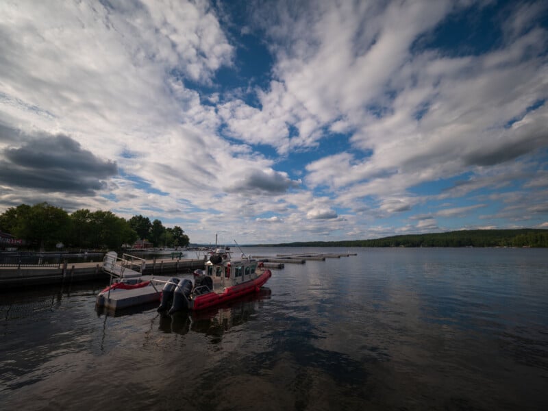 A red and white emergency response boat is docked at a pier on a calm lake under a cloudy sky.