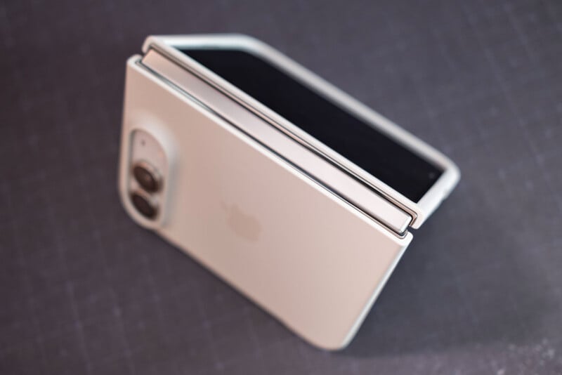 A white, foldable smartphone with a dual-camera system is partially folded and resting on a dark, grid-patterned surface.