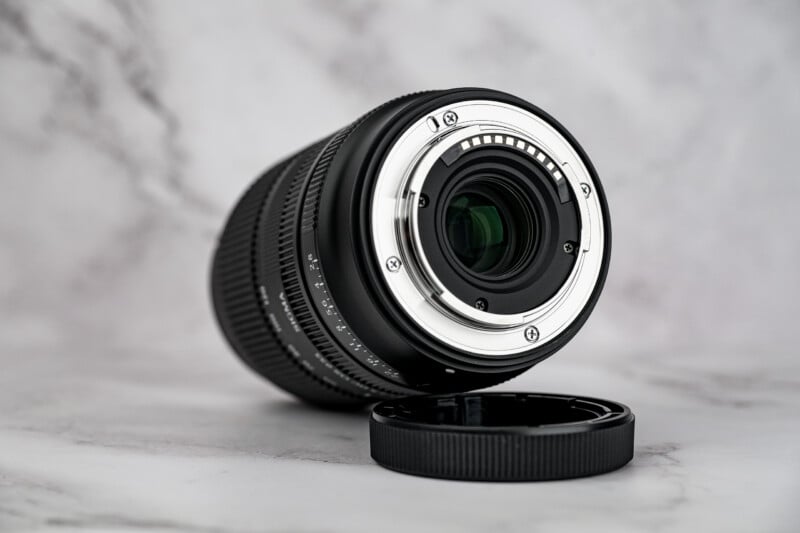 A black Sigma camera lens rests on a white marble surface next to its detached rear lens cap.
