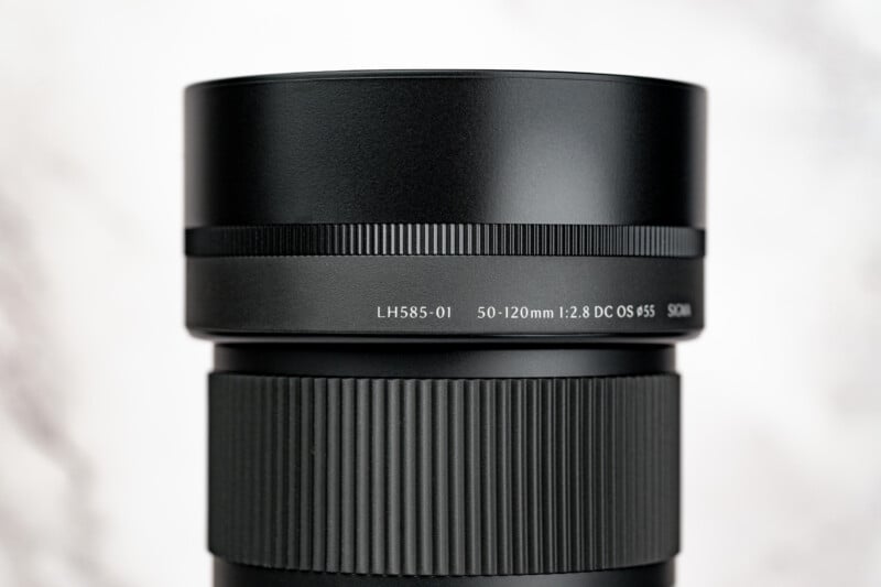 A close-up view of a black camera lens hood with the text "LH585-01 50-120mm 1:2.8 DC OS ø55 SIGMA" printed on its side.