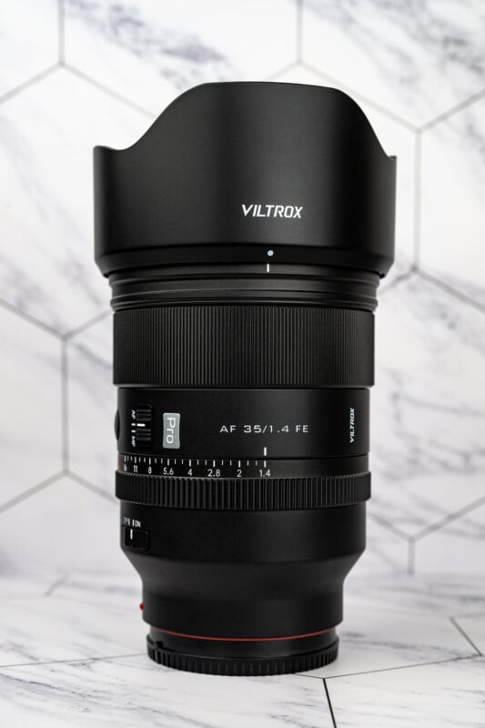 A black Viltrox AF 35/1.4 FE Pro camera lens stands upright against a white marble-patterned hexagonal tile background.