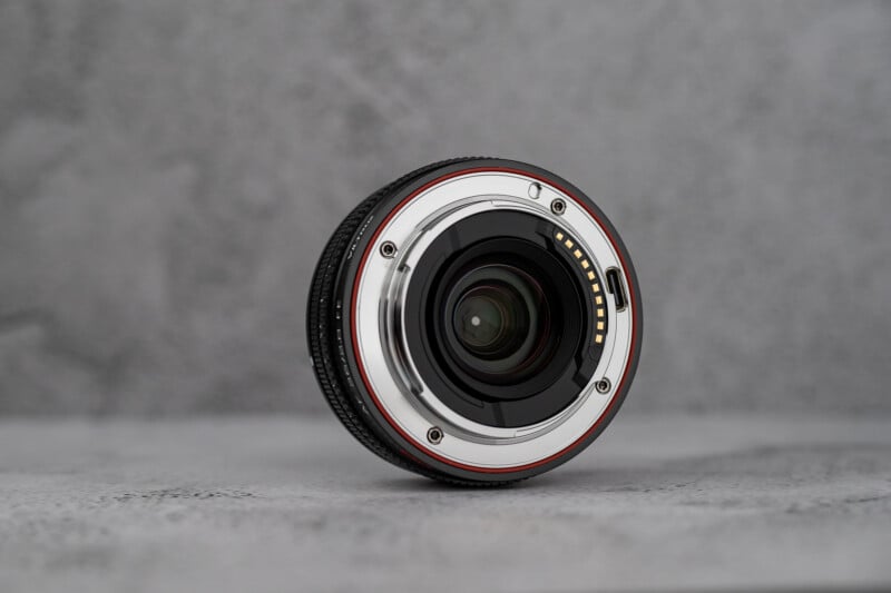 A Viltrox 50mm f/1.8 FE camera lens is shown from the rear mount perspective, resting on a textured gray surface.