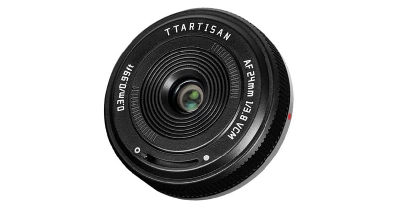 A black TTArtisan AF 24mm f/3.8 VCM pancake lens viewed from the front, showing the glass element and lens markings.