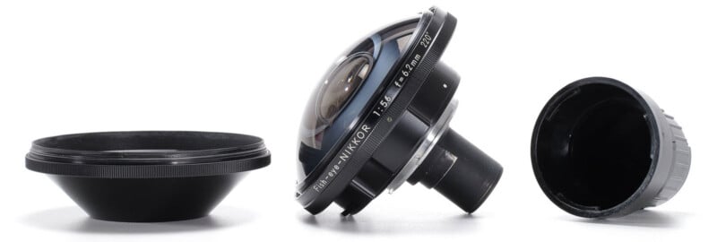A Fish-eye-Nikkor 6.2mm f/5.6 lens is positioned between its front lens cap on the left and its rear lens cap on the right.