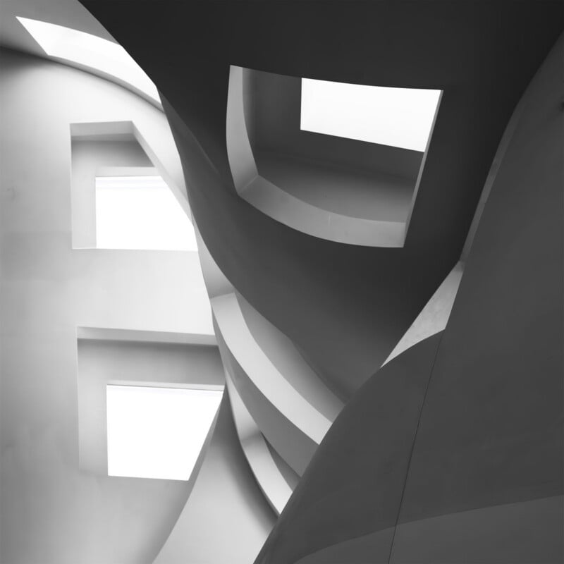 A black and white interior view of a modern building featuring curved, sculptural walls and rectangular skylights.