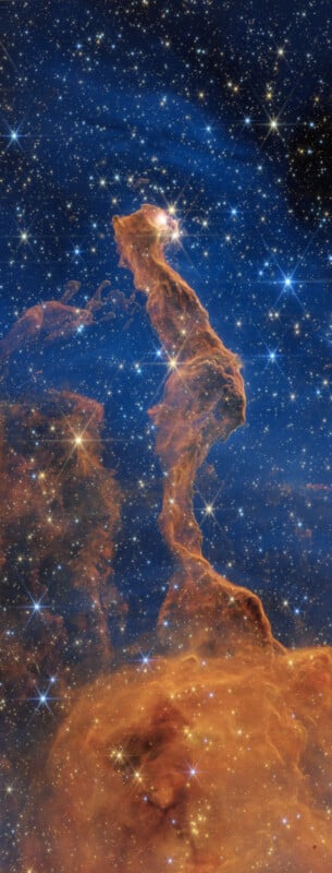 A towering, golden-brown pillar of interstellar gas and dust rises against a dense, star-filled blue background.