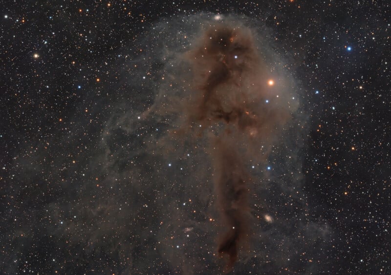 A dark, silhouetted nebula shaped like a human figure stands out against a bright, diffuse cloud of gas and a dense field of stars.
