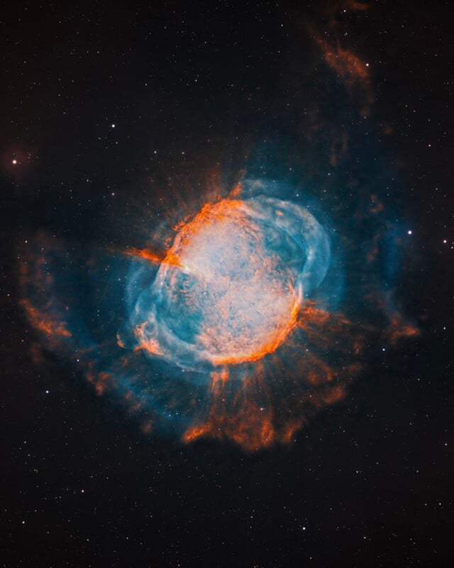 A vibrant nebula glows with orange and blue gas clouds against a dark, star-filled space background.