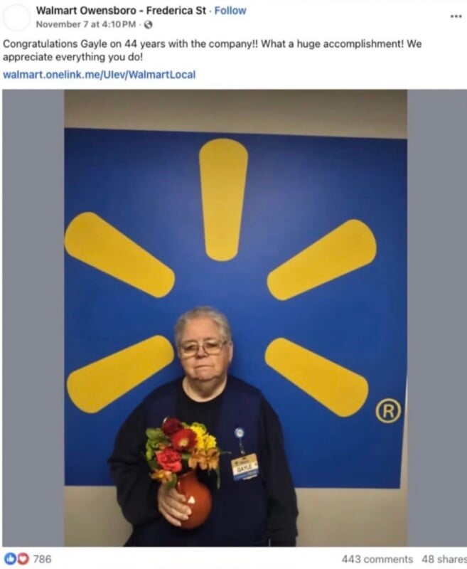 A woman named Gayle wearing a blue vest and name tag holds a small vase of flowers in front of a blue wall with a yellow Walmart spark logo.