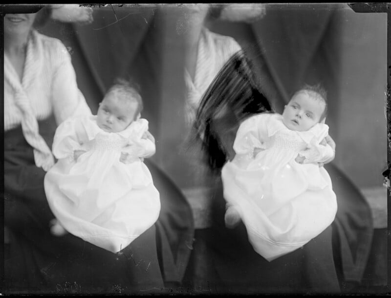 A double-exposure black and white portrait of a woman holding a baby in a white gown, with a large motion blur streak across the center.