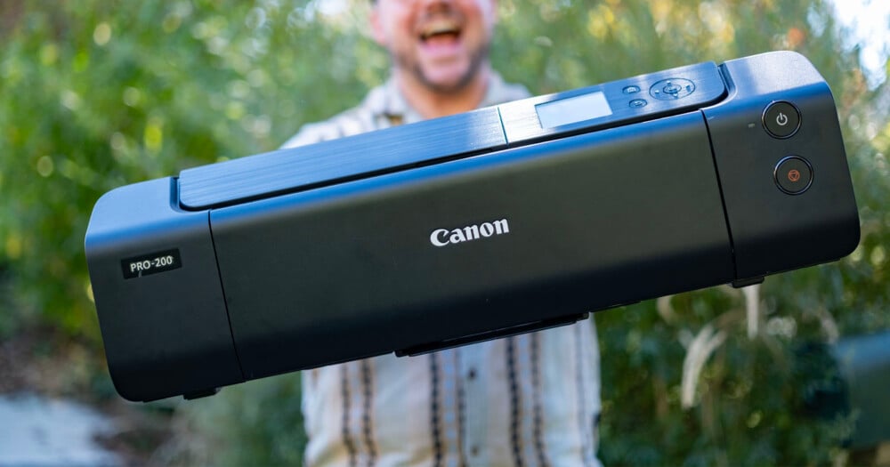 A person holds a black Canon PRO-200 printer in front of a blurred outdoor background.