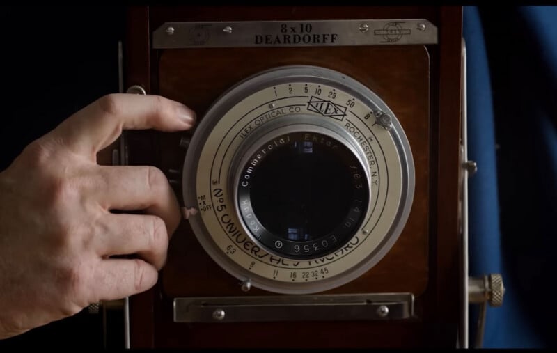 A hand adjusts the settings on the lens of a large-format Deardorff 8x10 camera.