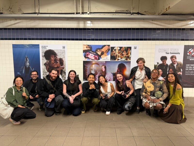 A group of eleven people pose for a photo in front of a subway wall decorated with various photographic prints.