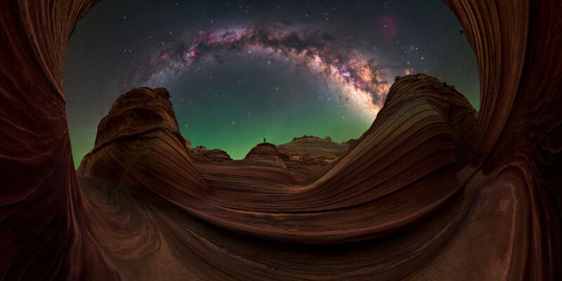 A person stands atop a sandstone formation surrounded by swirling, layered rock walls under a vibrant Milky Way galaxy.