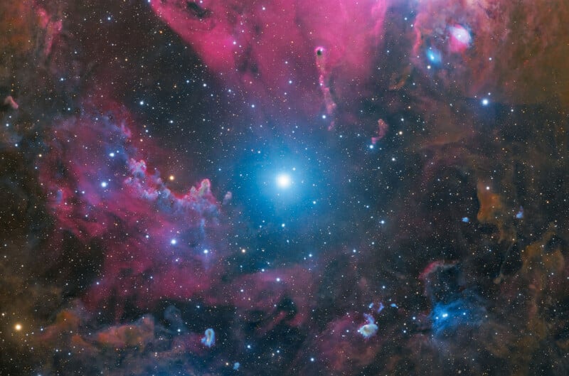 A bright, central blue star surrounded by vibrant pink and orange nebulae and a dense field of distant stars.