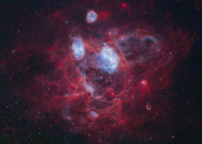 A vibrant nebula featuring glowing red gas clouds and bright blue star clusters set against a dark, star-filled background.