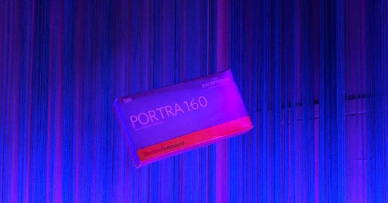 A box of Kodak Professional Portra 160 120 film floats against a background of vertical blue and purple string curtains.