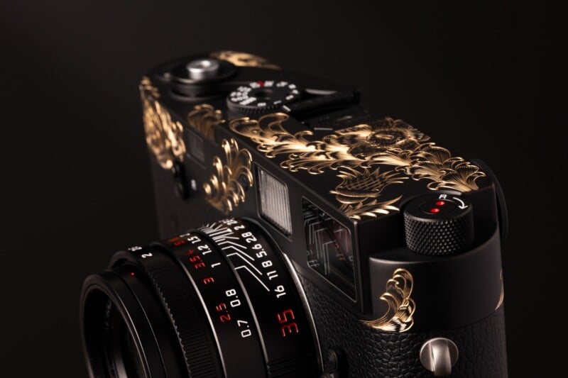 A black camera with gold floral engravings on the top plate and a lens featuring red numerical markings.