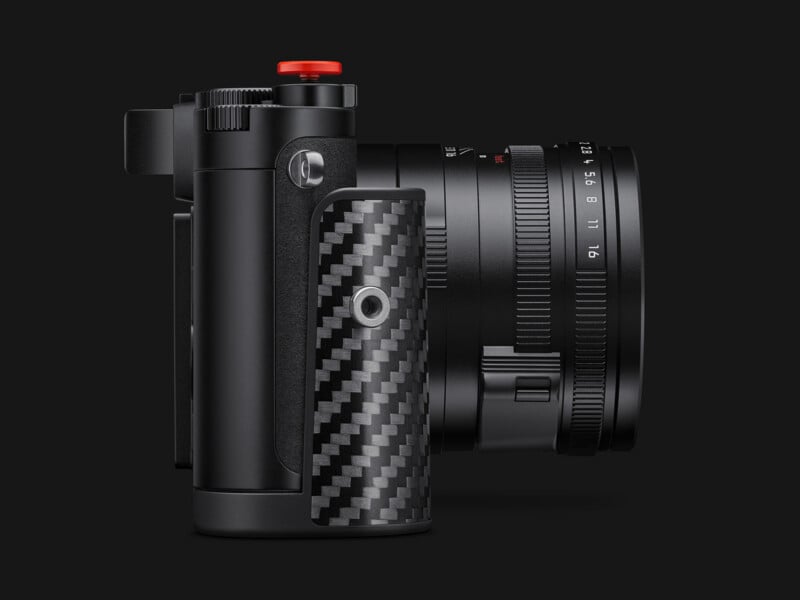A side view of a black camera with a carbon fiber grip, a red shutter button, and a lens with visible aperture markings.