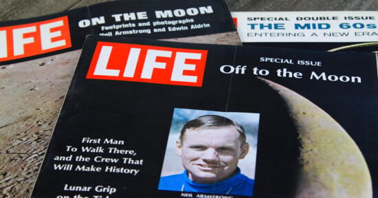 Three vintage LIFE magazine covers are arranged on a wooden surface, featuring headlines and imagery related to the Apollo moon landings and the 1960s.
