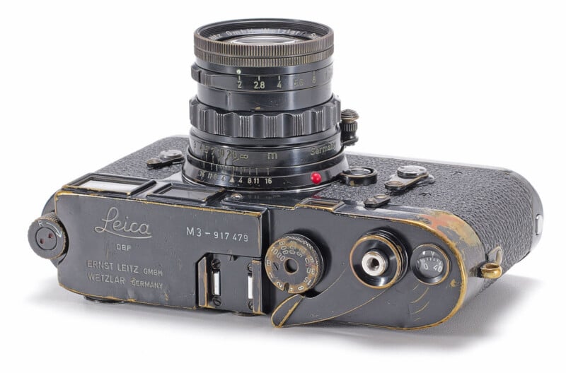 A black Leica M3 camera with a lens attached, showing significant brassing and wear on the top plate and body.