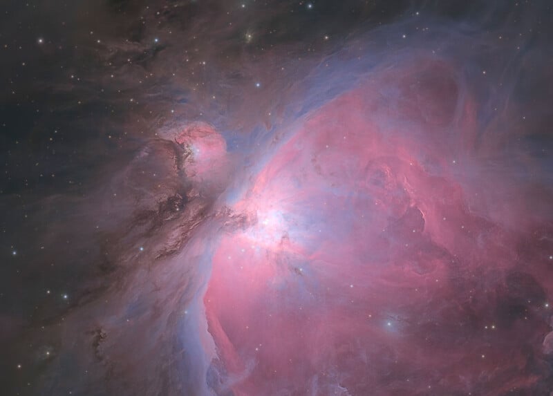 A vibrant nebula glows with swirling clouds of pink and blue gas, punctuated by scattered bright stars against a dark sky.