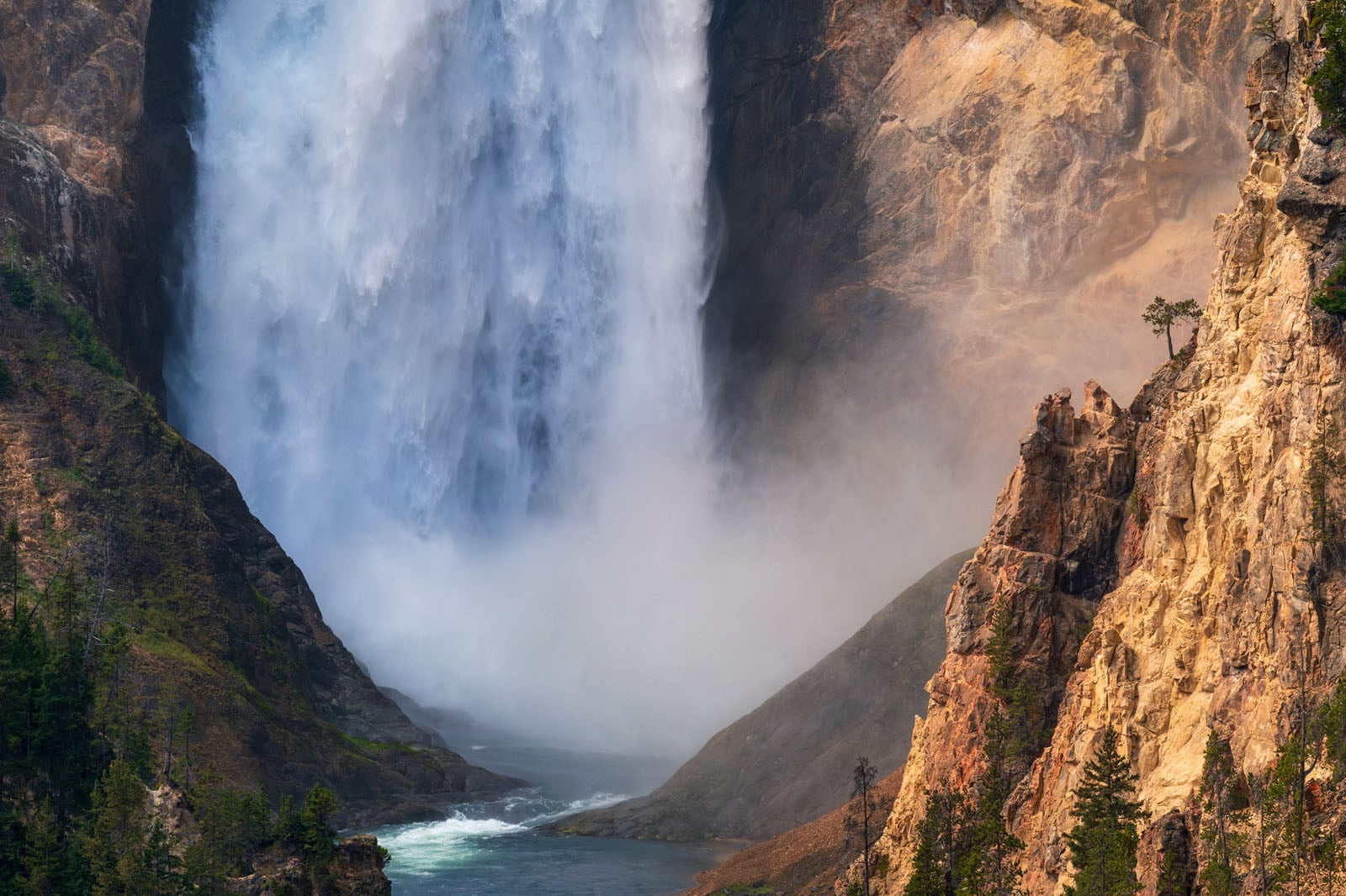 A powerful waterfall cascades into a deep, rocky canyon, creating a large cloud of mist at its base.