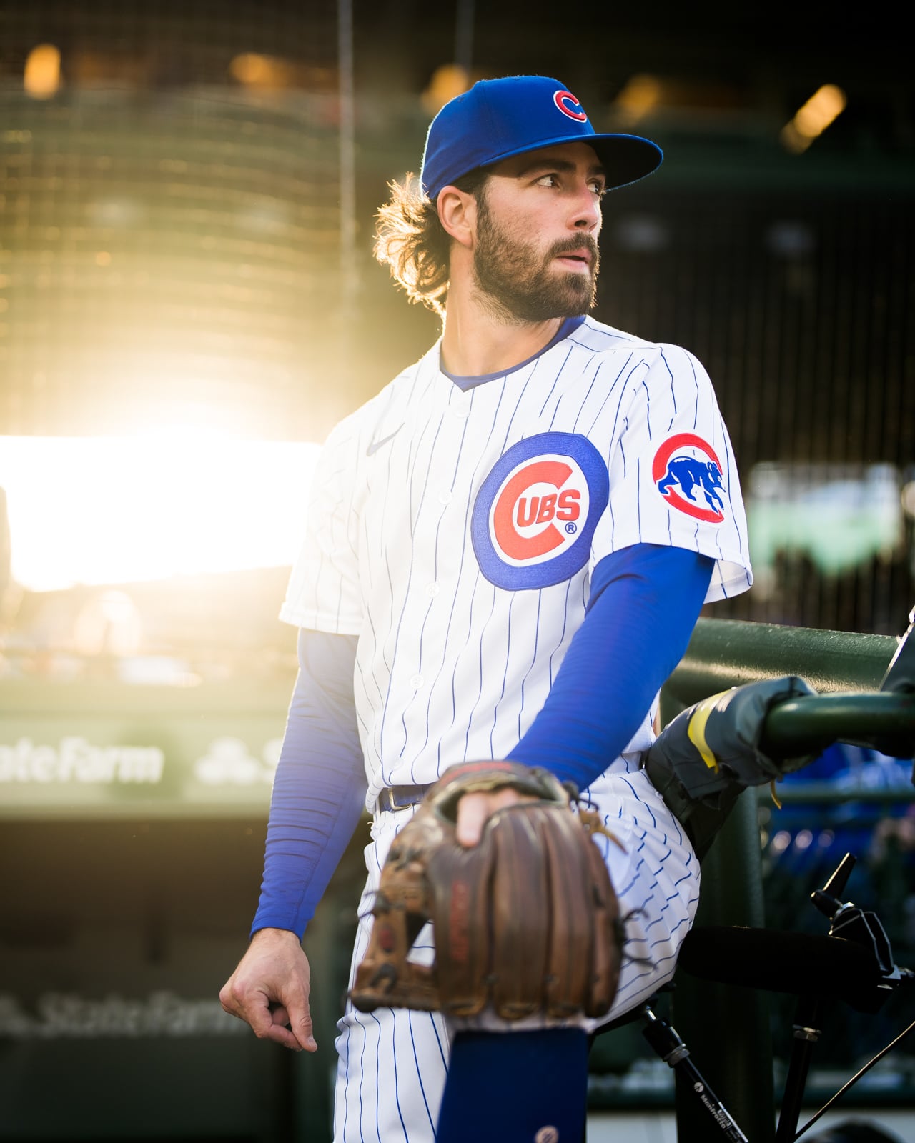 A baseball player wearing a Chicago Cubs uniform and cap stands in a dugout, holding a leather glove.