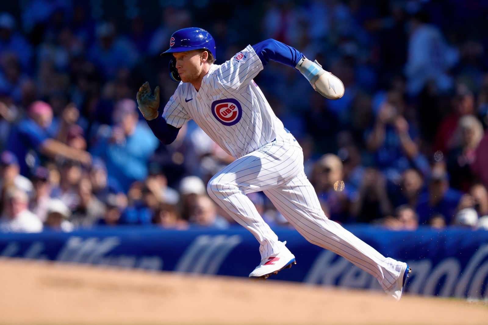 A Chicago Cubs baseball player in a white pinstriped uniform runs across the field during a game.