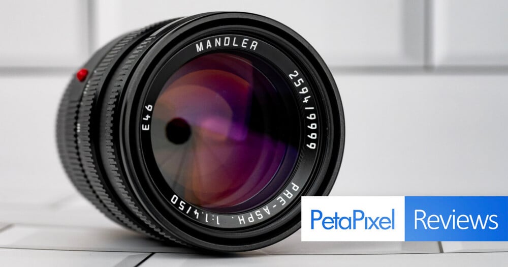 A close-up of a black camera lens with text on the front element reading "MANDLER," "2594/19999," "E46," and "PRE-ASPH. 1:1.4/50," with a PetaPixel Reviews logo in the bottom right corner.
