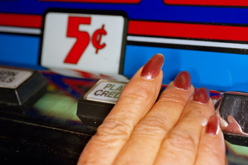 A hand with dark red nail polish rests on the "Play Credits" button of a 5-cent slot machine.