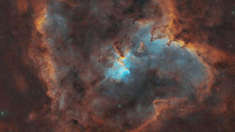 A vibrant nebula featuring glowing clouds of orange and blue gas, with a bright, concentrated cluster of stars at its center.