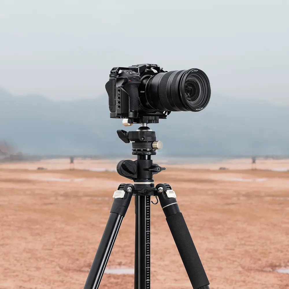 A black camera with a lens mounted on a tripod stands in a desert landscape with mountains in the background.