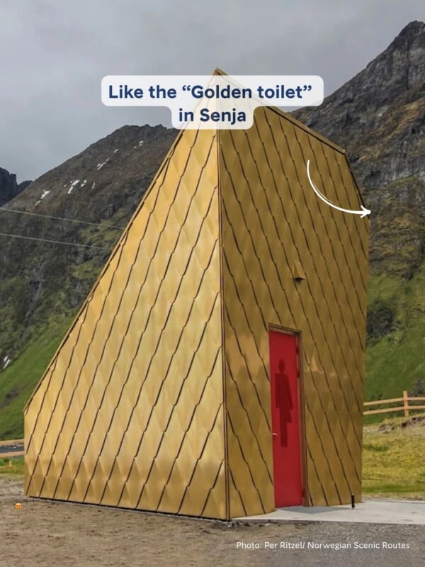 A gold-colored, angular public restroom building with a red door stands against a backdrop of mountains.